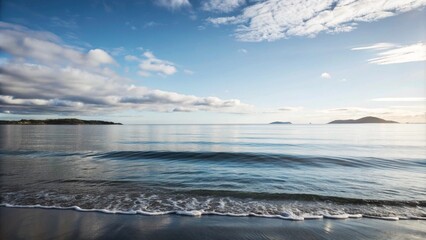 Fototapeta premium Calm ocean waves lapping on a sandy shore under a clear blue sky.