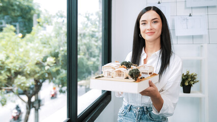 Close up of skilled young beautiful caucasian architect lift house model left side and right sight...