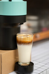 Coffee machine with capsules preparing cappuccino in transparent glass at domestic kitchen at home. Espresso caffeine beverage maker and creamy italian drink