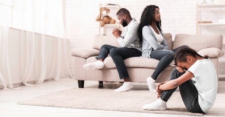 Family problems concept. Sad little afro girl sitting with her head on knees, tired of parents...