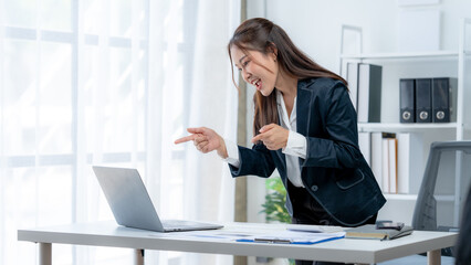 Asian businesswoman smiling happily while working on laptop at table in office