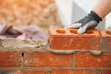 Skilled Bricklayer Placing Brick on Wall at Construction Site in Daylight