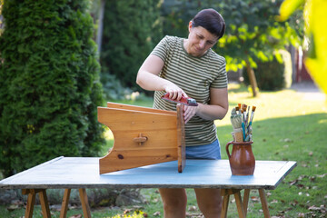 Woman painting a wooden furniture outdoors, an eco-friendly re-use business.