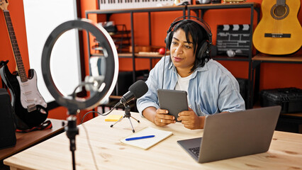 A middle-aged woman records a podcast in a music studio, with a microphone, tablet, laptop, and...