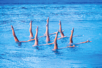 Synchronized female artistic swimming team performing synchronized legs movement in swimming pool