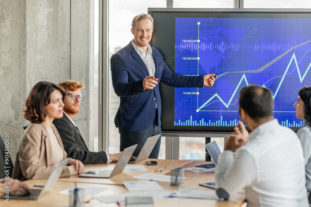 Fototapete a businessman stands in front of a large screen displaying a graph with an upward trend, pointing to