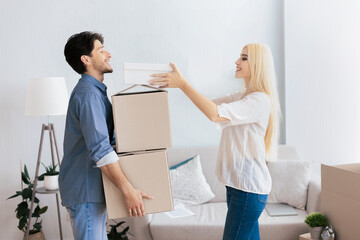 A woman hands a box to her partner while they unpack boxes in their new apartment.