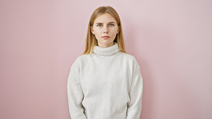 Serene caucasian woman with blonde hair, blue eyes, wearing a white sweater isolated against a pink background