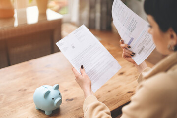 Woman Reading Financial Documents While Sitting at a Wooden Table With a Piggy Bank Nearby