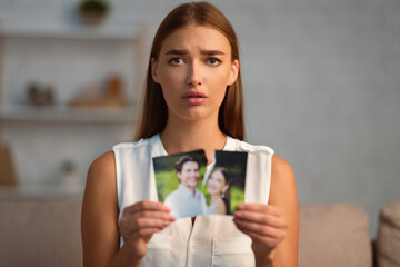 Divorce. Upset Woman Tearing Apart Wedding Photo With Ex-Husband After Breakup Sitting On Sofa...