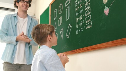 Happy caucasian boy writing answer at blackboard and thinking about theory while standing in front...