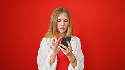 A focused young woman with blonde hair uses a smartphone against a vibrant red background.
