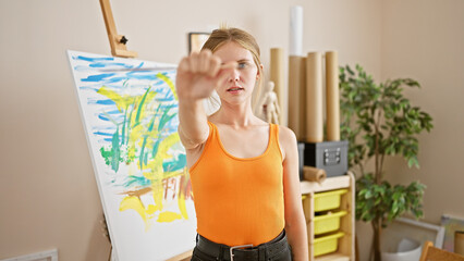 A focused young woman artist in a studio observes her colorful painting, showcasing creative expression and artistic passion.
