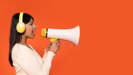 Woman Wearing Headphones Yelling Into Megaphone Against Bright Orange Background