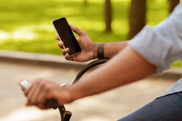 Ride Navigation. Unrecognizable afro man riding bike and holding smartphone with black screen, using online maps app, cropped image, closeup