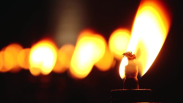 A close up shot of a line of lit torches, their flames glowing warmly in the dark night. The foreground torch is in sharp focus, while the others blur into the background, creating a serene