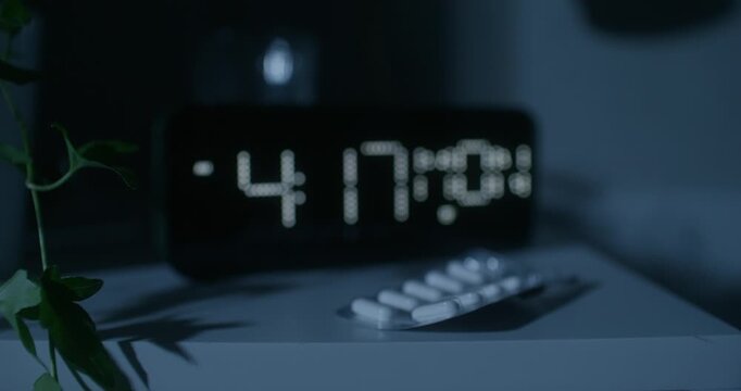 The luminous dial of the clock at home. The pills are on the bedside table. Night time, dark room