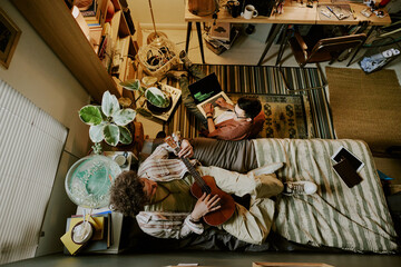 Top view of two students spending free time in dorm room and talking while improving guitar playing...