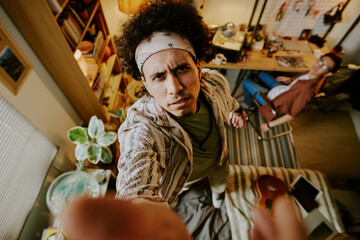 Curly-haired man with black and white bandana putting security camera while standing on bed in dorm room