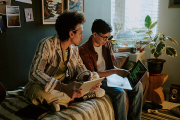 Friends startupers sitting on bed while discussing last codes for their brand new application