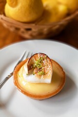 Bery beautiful and tasty lemon tartelette with meringue on a white plate, on a white plate, next to a pannier with lemons. The best typical French baking.