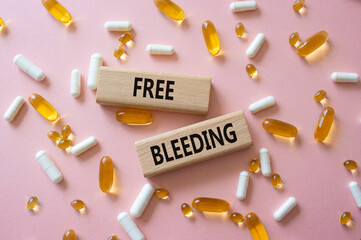 Free bleeding symbol. Concept words Free bleeding on wooden blocks. Beautiful pink background with pills. Motivational and Free bleeding concept. Copy space.