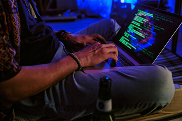 Unrecognizable male hands typing code on black keyboard with neon rays