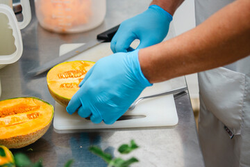 Chef removing seeds from melon using a spoon wearing blue gloves