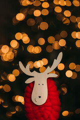 A wooden figure of a reindeer with a red knitted trunk on the background of a Christmas tree and...