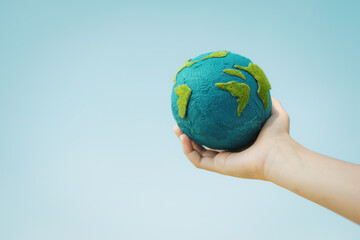 Young boy's hand holding planet Earth globe with sky and cloudscape background as Earth day to save...