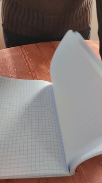 Primer plano de unas hojas de papel con cuadros de un cuaderno escolar en movimiento sostenido por unas manos. Video vertical.
