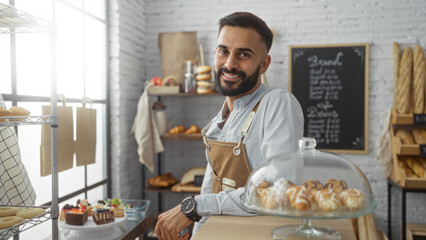 Handsome young hispanic man with beard smiling in bakery shop interior with bread and pastries in the background
