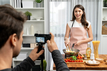Cameraman recording to woman in chef influencer host cooking spaghetti with meat topped tomato...