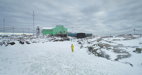 Man running polar research station on Antarctica coastline, Vernadsky science base. Green house buildings on rocky ocean coast. Antarctic expeditions and travel. South Pole exploration. Drone flight