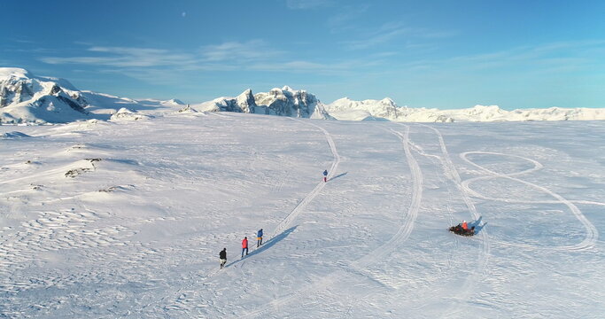 People enjoy outdoor sport activity in Antarctica. Group of scientists from polar station run snow trail race. Travel, active lifestyle, recreation in arctic wild nature landscape. Aerial drone shot