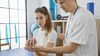 Fototapeta premium A male therapist in a clinic assists a focused woman with her hand rehabilitation exercises indoors.