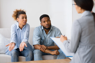 Disagreement In Relationship. Black Couple Discussing Family Issues With Psychologist Sitting On Couch