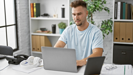 Handsome young hispanic man with beard working on laptop in a modern office setting.