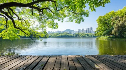 Obraz premium A tranquil urban lake reflects the skyline, framed by trees and vibrant greenery under a clear blue sky on a sunny day