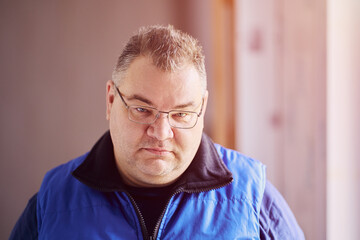 Frowning look from under eyebrows, large chubby-cheeked Caucasian man with glasses looks angrily.