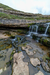 Picturesque waterfall flowing over layered rock formations with lush green moss in Cantabria, Spain. Ideal for nature, travel, and landscape themes.