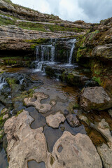 Picturesque waterfall flowing over layered rock formations with lush green moss in Cantabria, Spain. Ideal for nature, travel, and landscape themes.