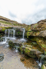 Picturesque waterfall flowing over layered rock formations with lush green moss in Cantabria, Spain. Ideal for nature, travel, and landscape themes.