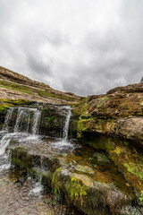 Picturesque waterfall flowing over layered rock formations with lush green moss in Cantabria, Spain. Ideal for nature, travel, and landscape themes.