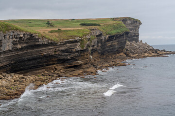 Majestic coastal cliffs with layered rock formations and lush greenery overlooking the sea in...