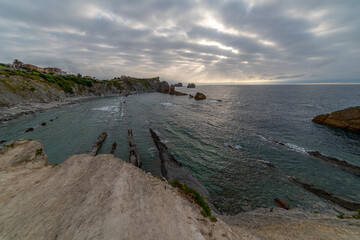 Beautiful sunset over Playa de la Arn&iacute;a, featuring dramatic skies, rocky shoreline, and coastal homes in Cantabria, Spain. Perfect for seascape, travel, and nature themes.