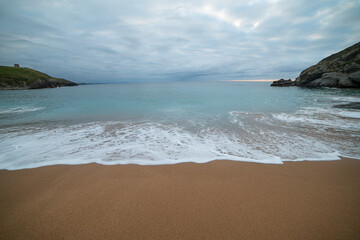 Tranquil scene of Tagle Beach in Cantabria, Spain, showcasing rugged rocks, gentle waves, and an expansive horizon. Perfect for travel, nature, and coastal themes.