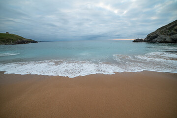 Tranquil scene of Tagle Beach in Cantabria, Spain, showcasing rugged rocks, gentle waves, and an expansive horizon. Perfect for travel, nature, and coastal themes.