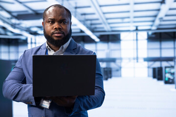 Programmer in data center using laptop to identify and solve technical issues related to data...