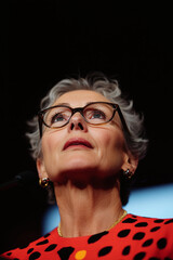 Obraz premium Elegant Senior Woman with Glasses Gazing Upward, Dramatic Lighting Portrait, Professional Leadership and Vision Concept